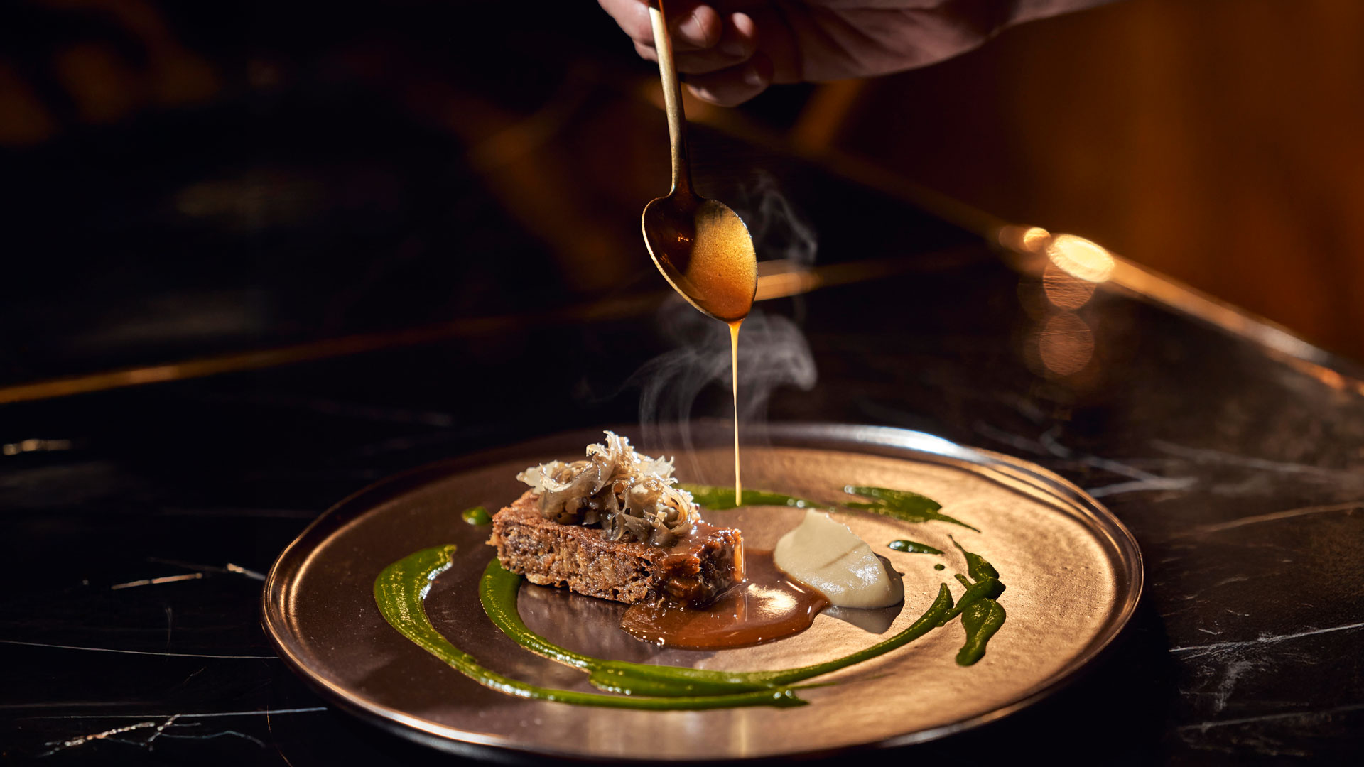 Koch richtet an und gießt dabei Sauce über ein Gericht mit verschiedenen Texturen im Stil der zeitgenössischen Küche.