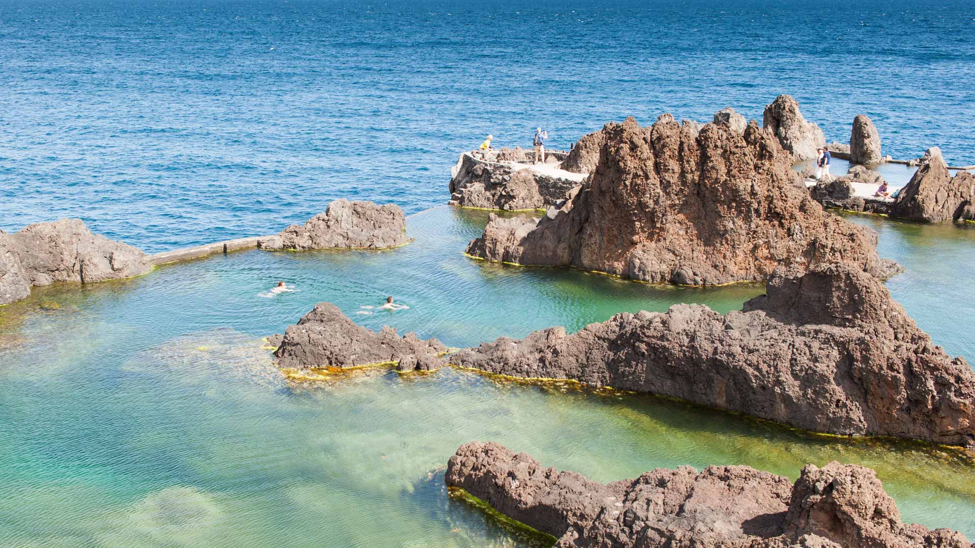 Menschen schwimmen in einem Naturpool, umgeben von Felsen auf Madeira.