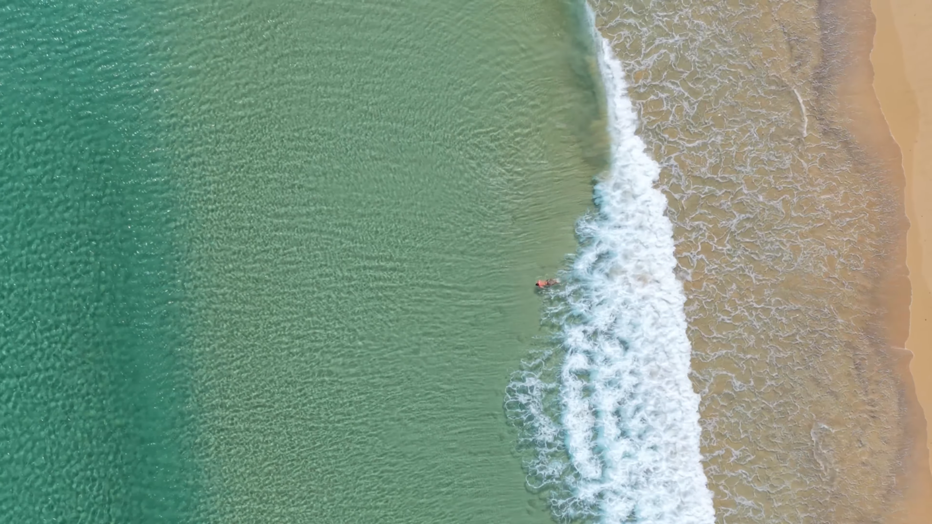 Mann beim Schwimmen im Meer von Porto Santo, mit sanften Wellen, klarem Wasser und Sandstrand.