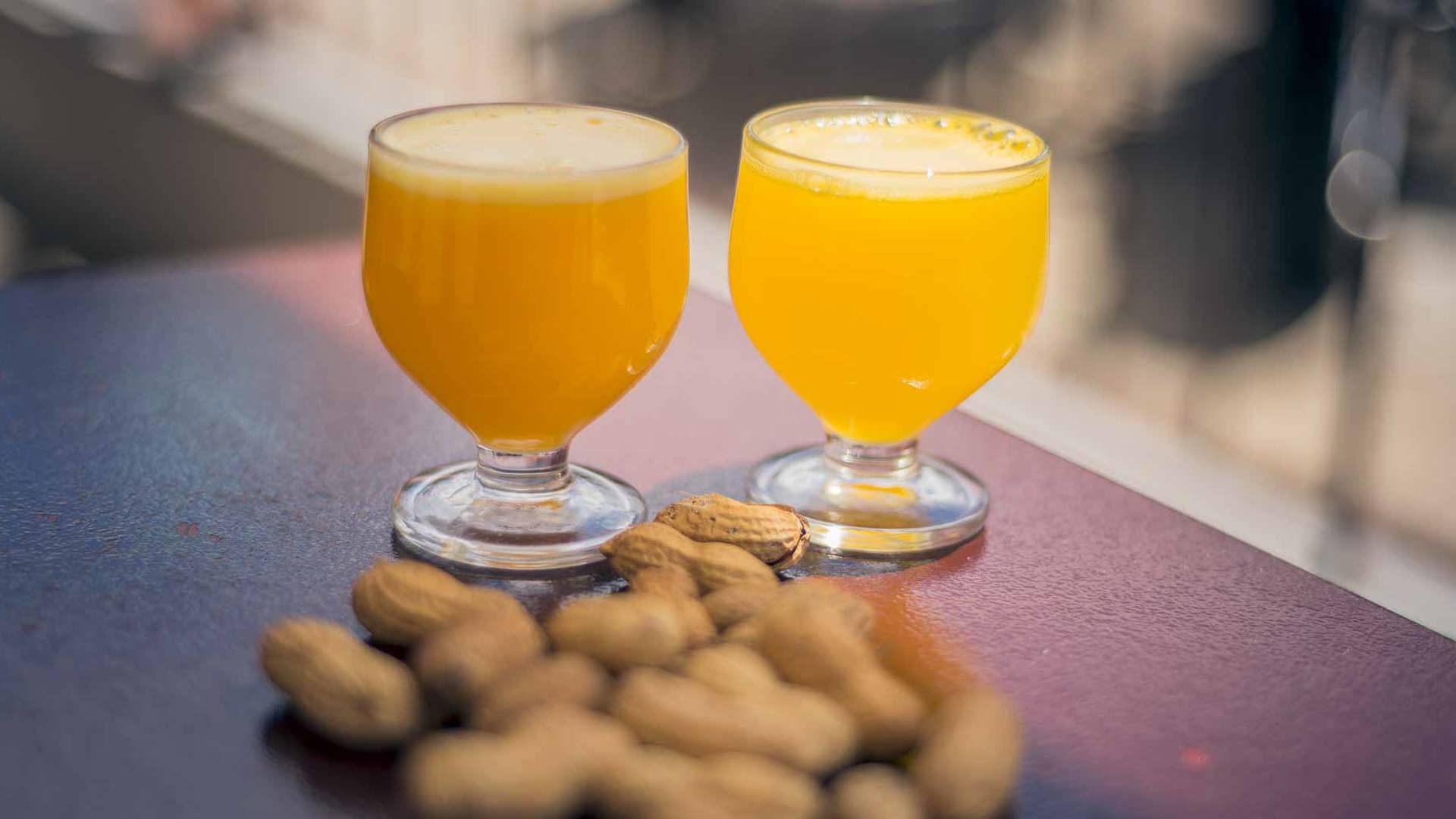 Two glasses of traditional Madeira poncha served with peanuts on a counter.