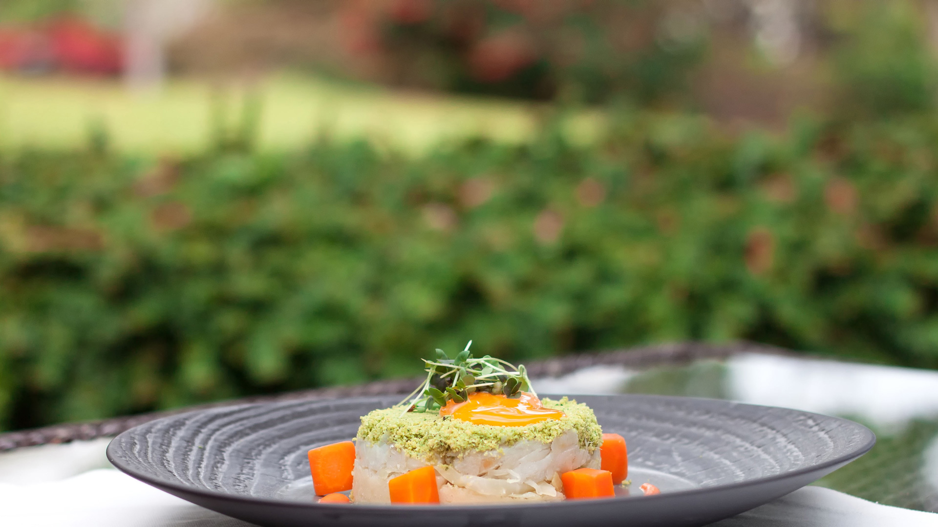 Black plate with round-shaped food, topped with green elements and carrot cubes.