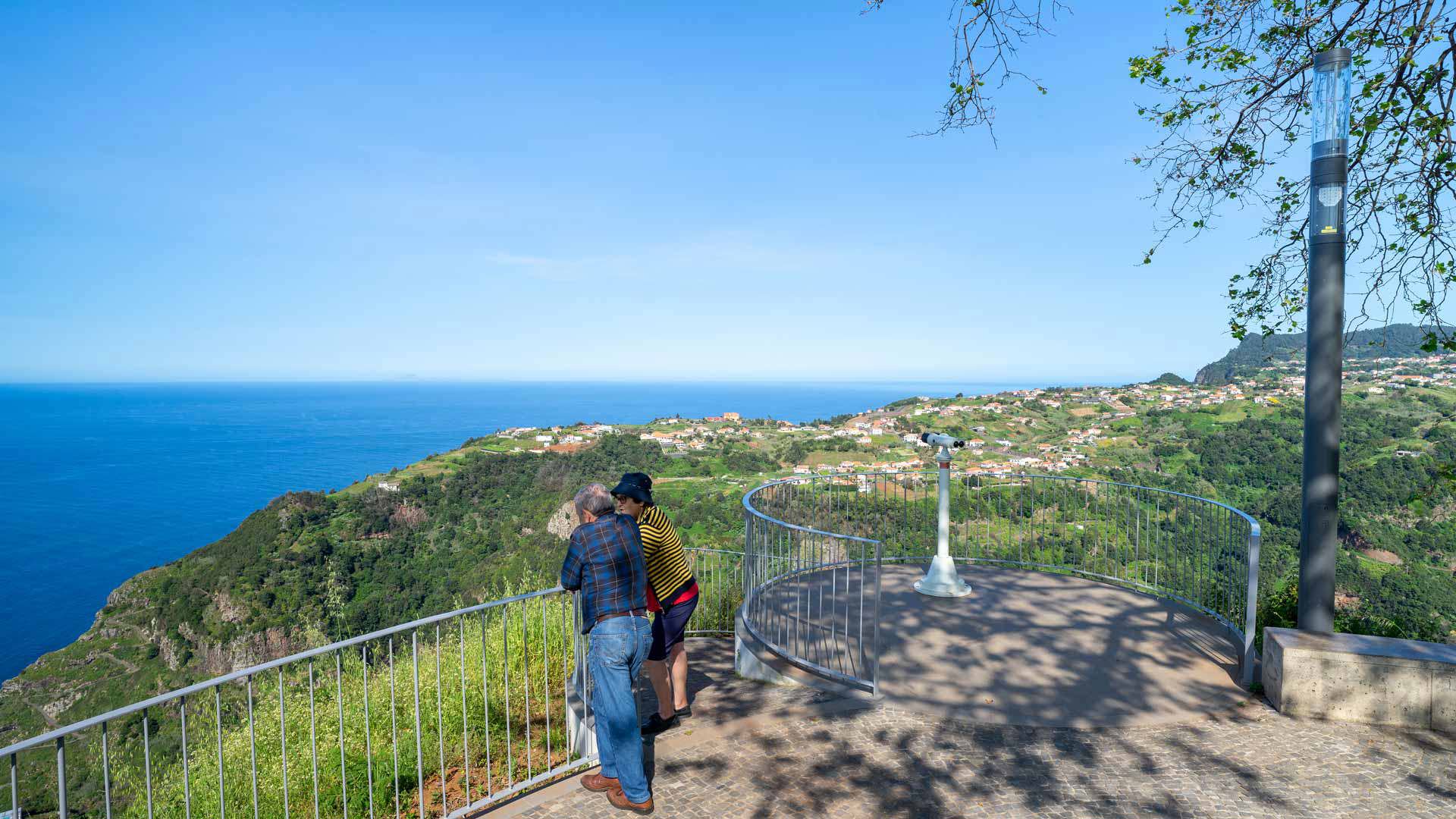 Two people at viewpoint with iron fence and telescope in Madeira.