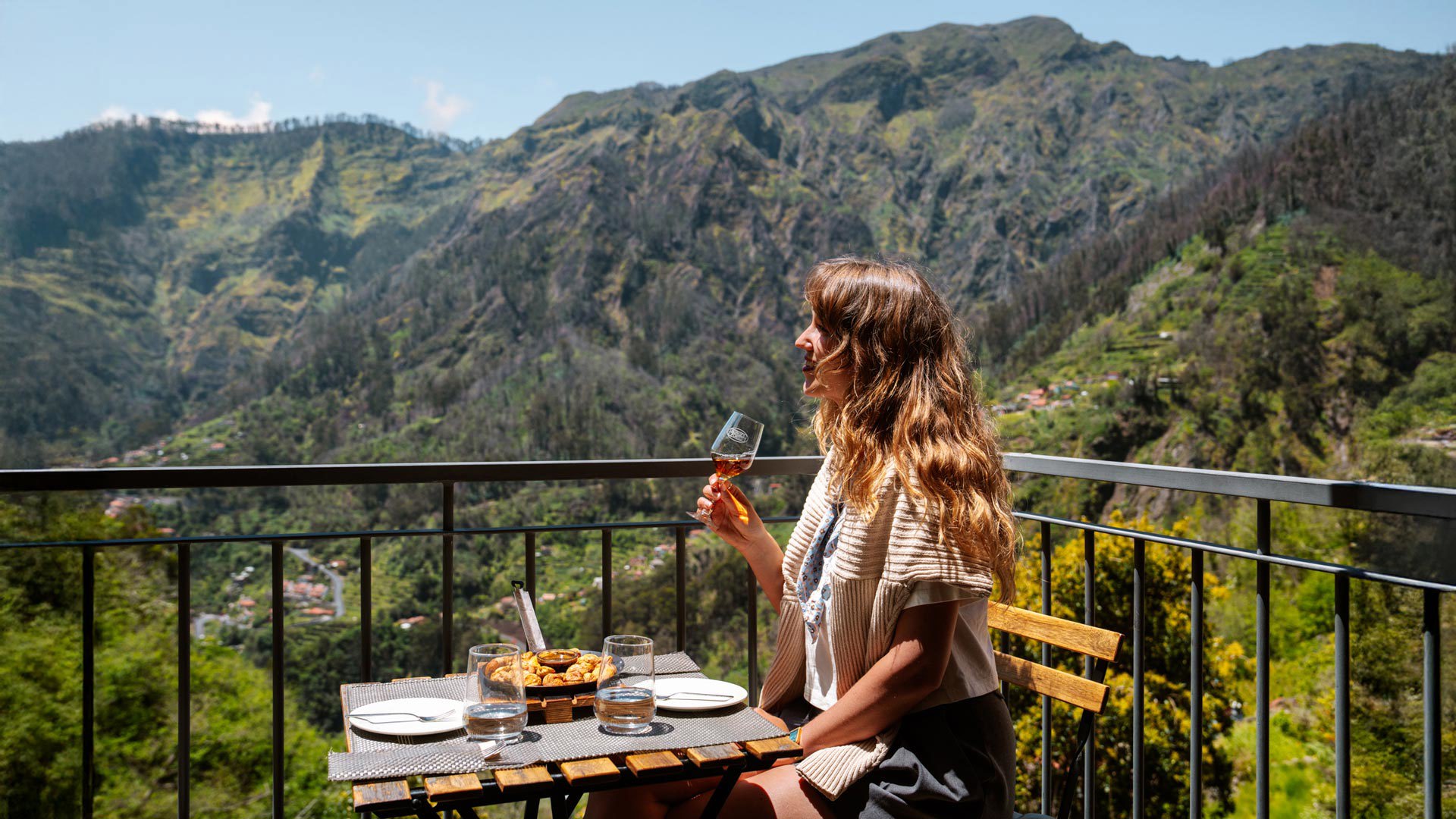 Frau beim Mittagessen auf einer Terrasse im Curral das Freiras, umgeben von Bergen und Vegetation.