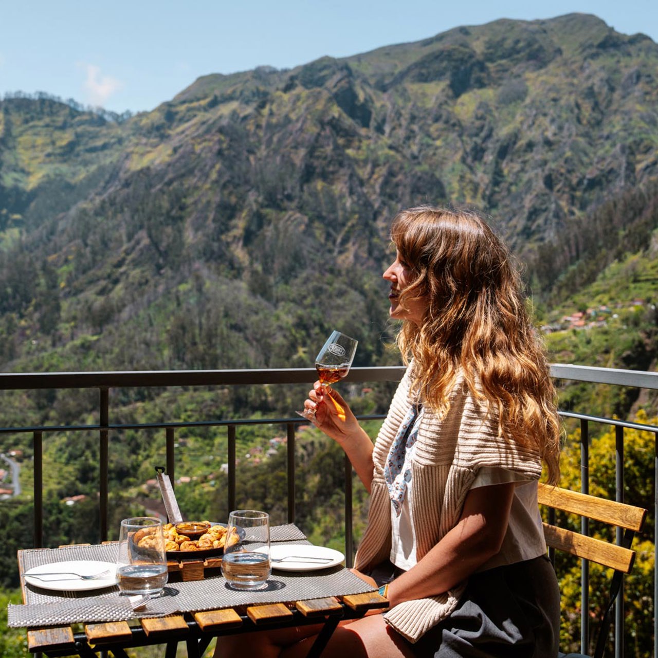 Mujer almorzando en una terraza en el Curral das Freiras, rodeada de montañas y vegetación.