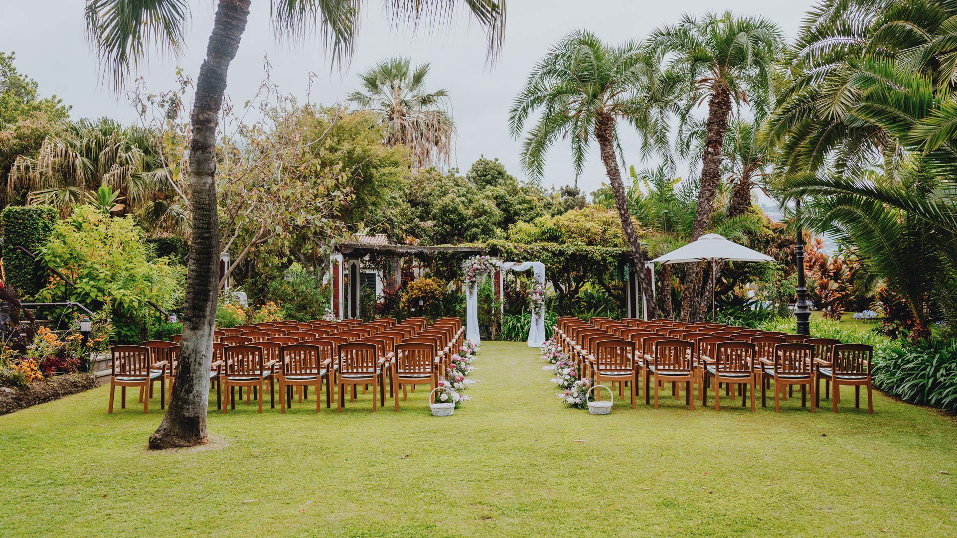 Outdoor wedding ceremony space with aligned chairs and decorated arch, surrounded by nature.