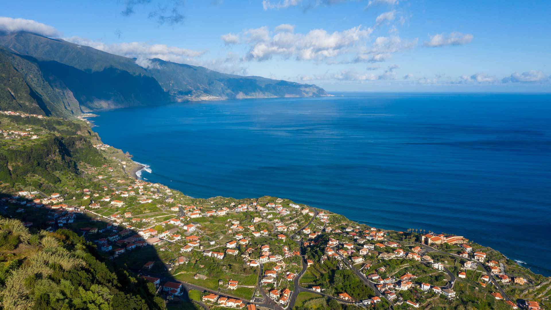 Casas num vale com mar e montanha ao fundo.