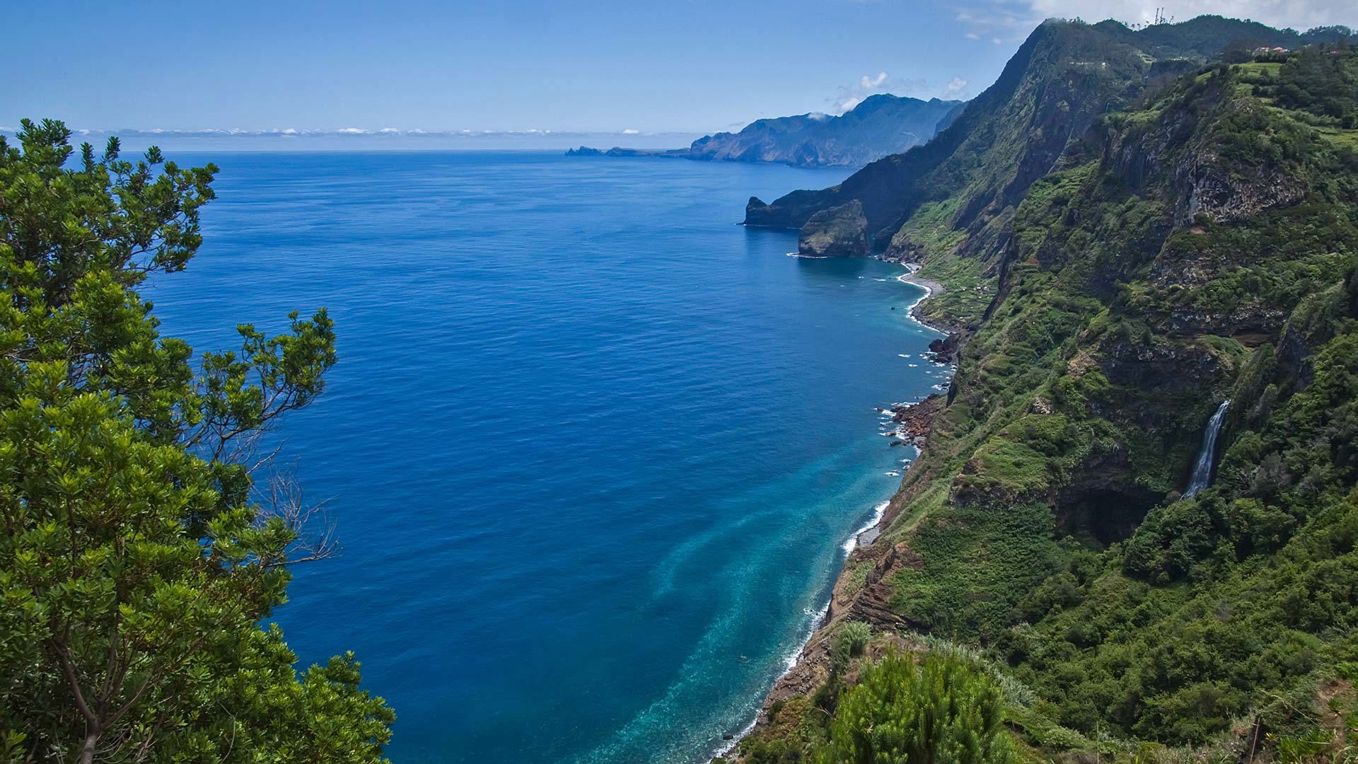 Green hillside with a waterfall by the sea in Madeira.