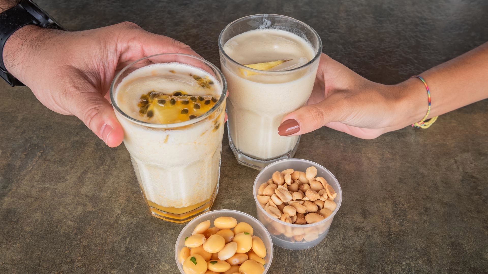 Zwei Hände halten zwei Gläser Nikita mit Snacks, typische Getränke von Madeira.