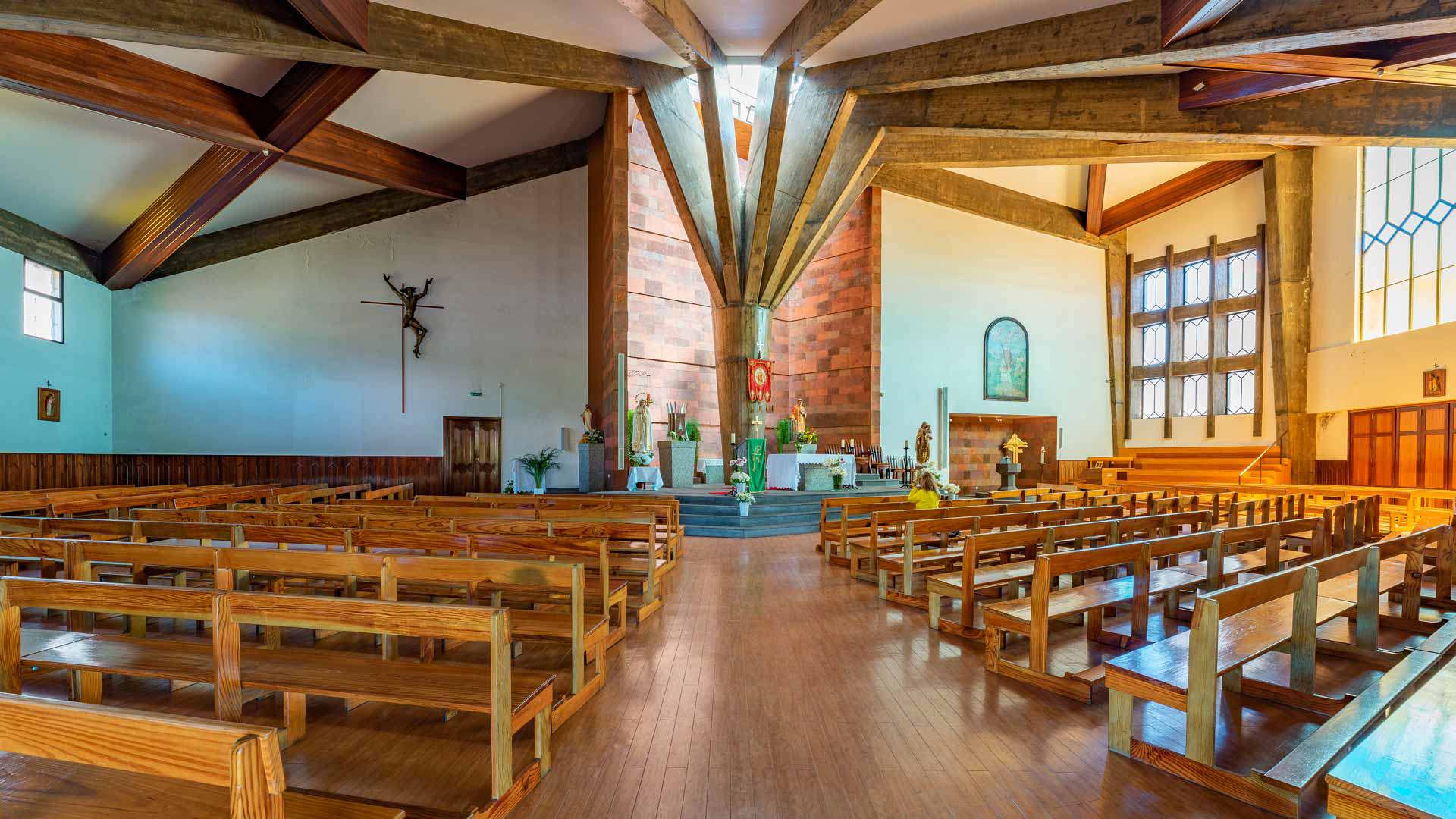Intérieur d’église avec bancs en bois, autel, piliers et vitraux colorés.