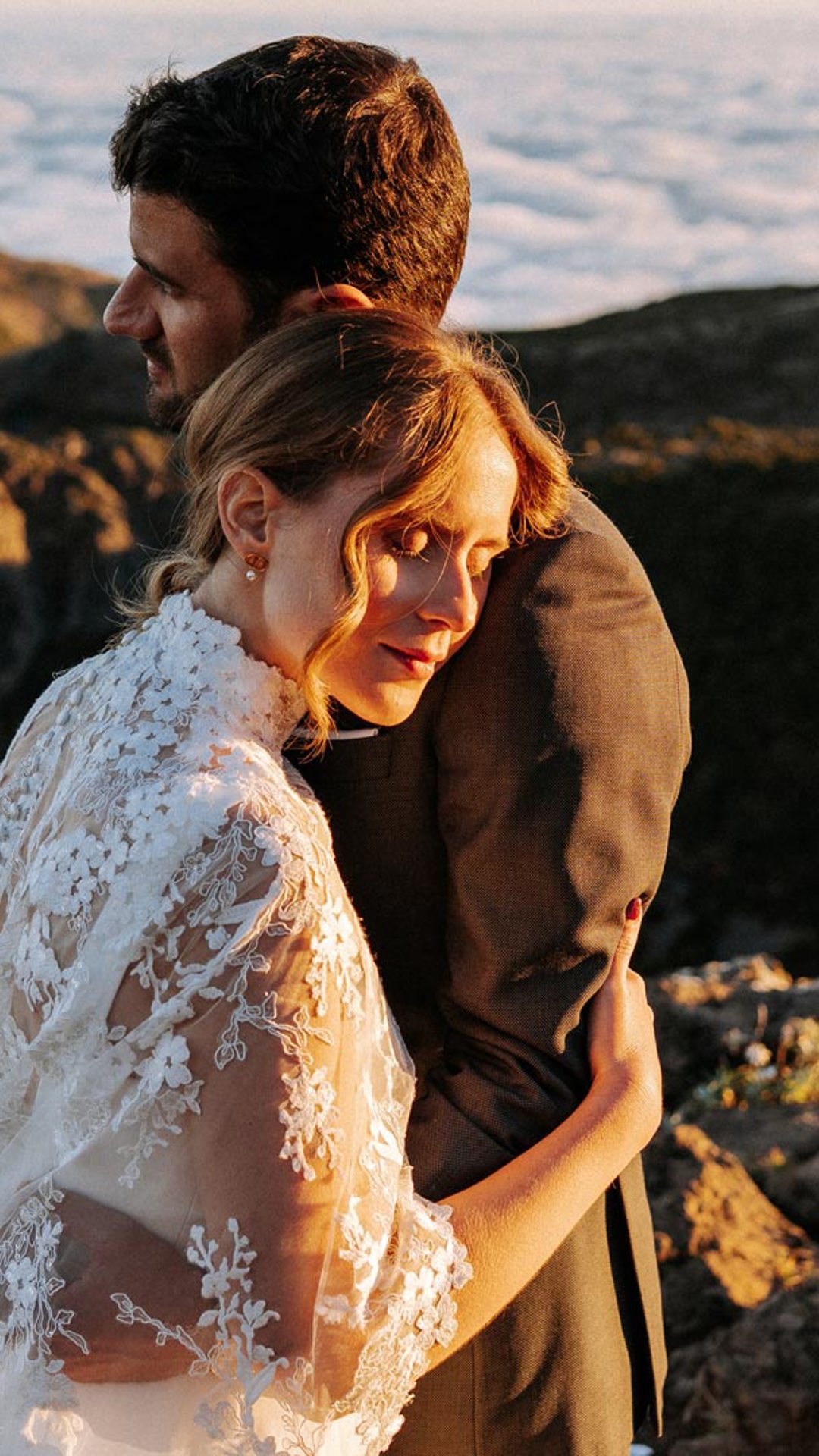Pareja con atuendos de boda en las montañas, sobre las nubes, abrazados.