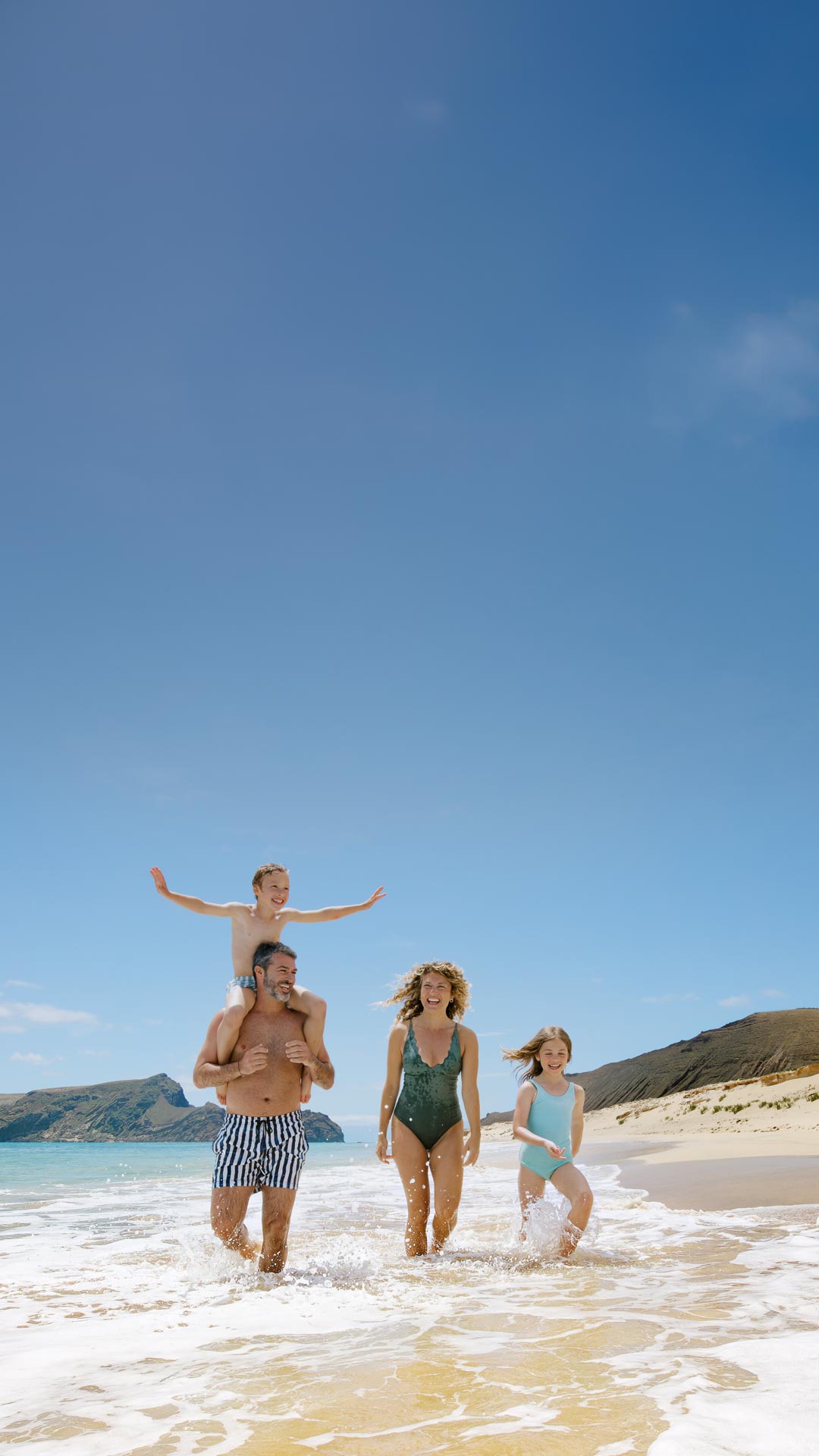 uma família a passear à beira-mar numa praia de areia 