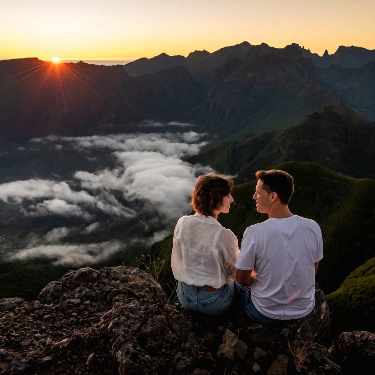 Couple watching the sunrise in the mountains, above the clouds.
