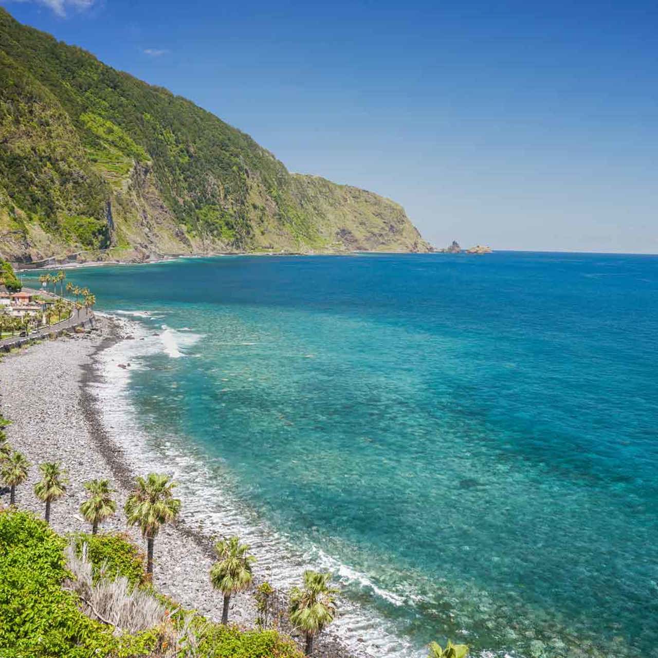 Plage de galets au bord de la mer, avec montagne et pente verte à Madère.