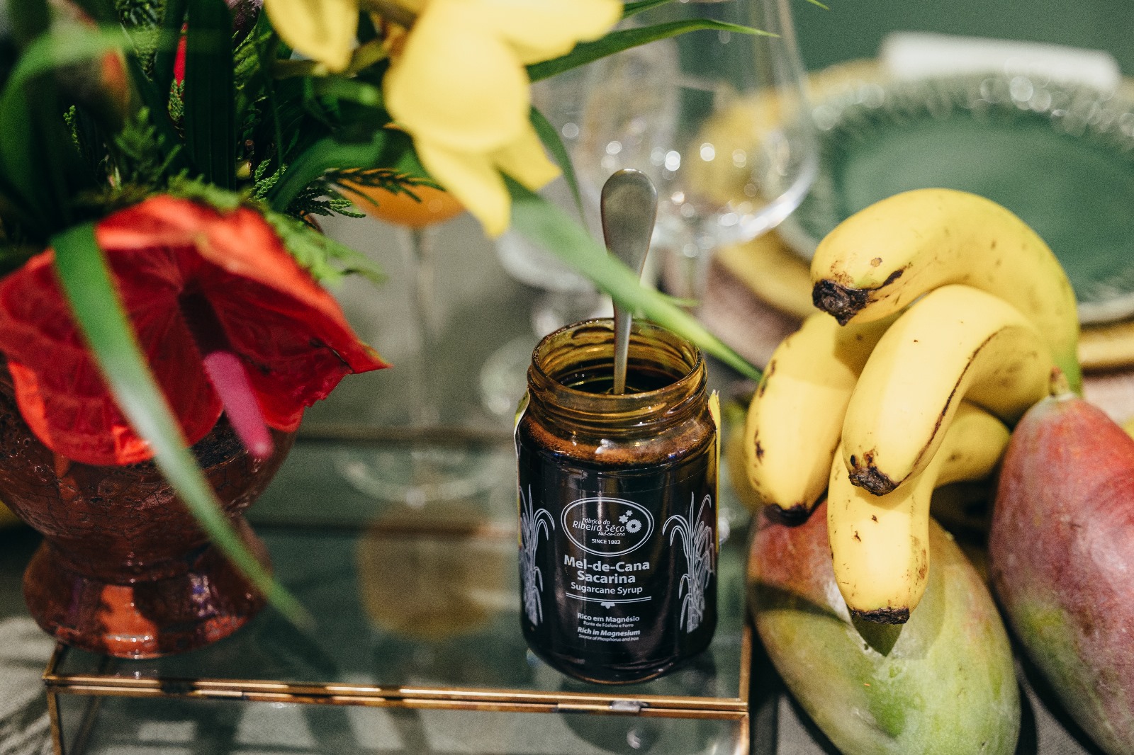 Jar of sugarcane honey in the foreground with bananas in the background.