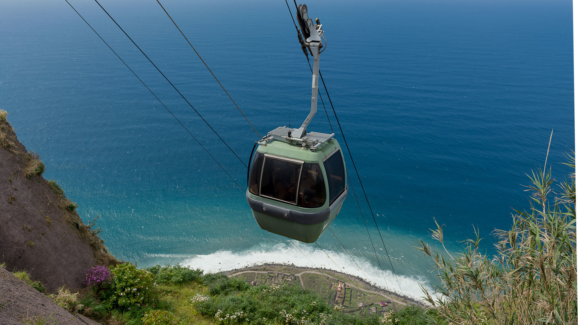 Seilbahn fährt über Hang mit Meerblick.