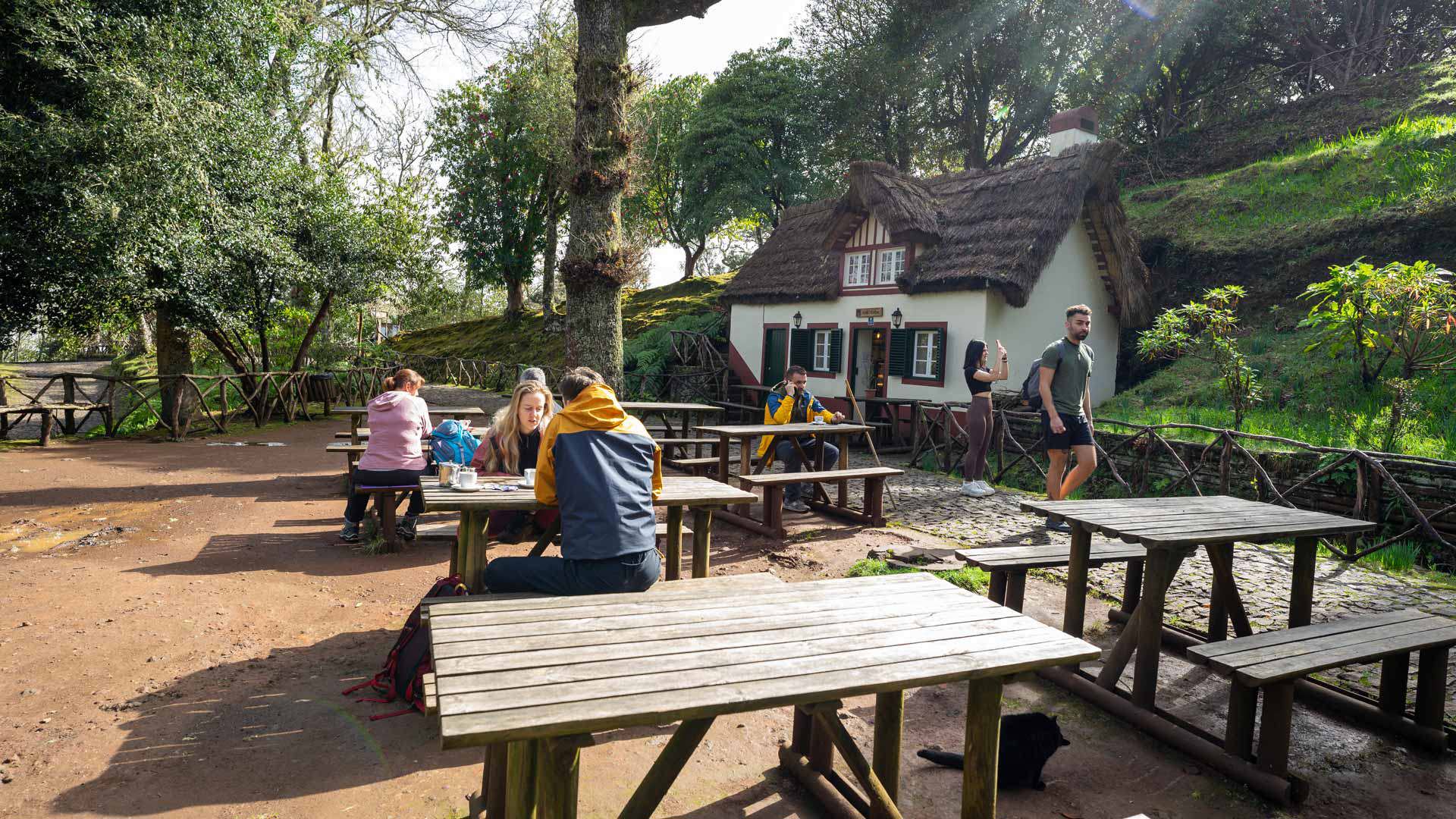 Pessoas sentadas em mesas de piquenique junto a casa em meio à natureza na Madeira.