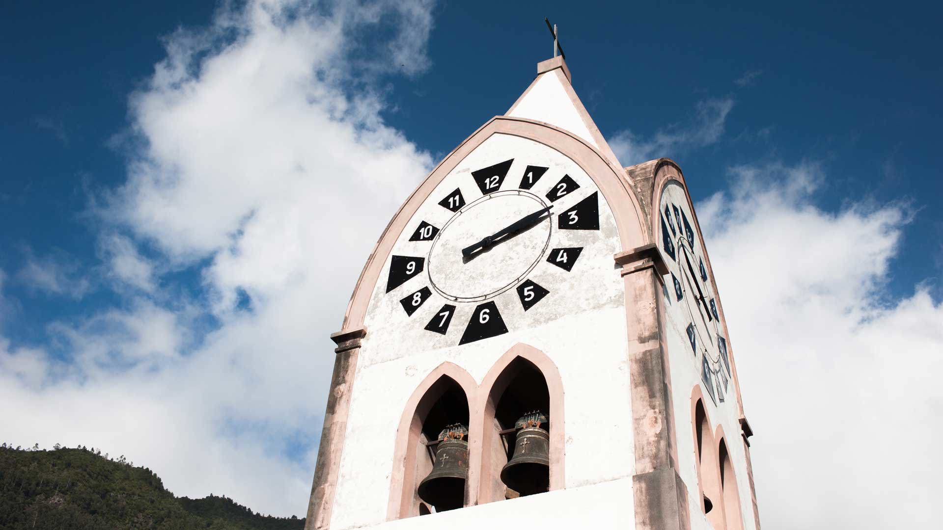 Torre con reloj de iglesia bajo cielo azul con nubes.