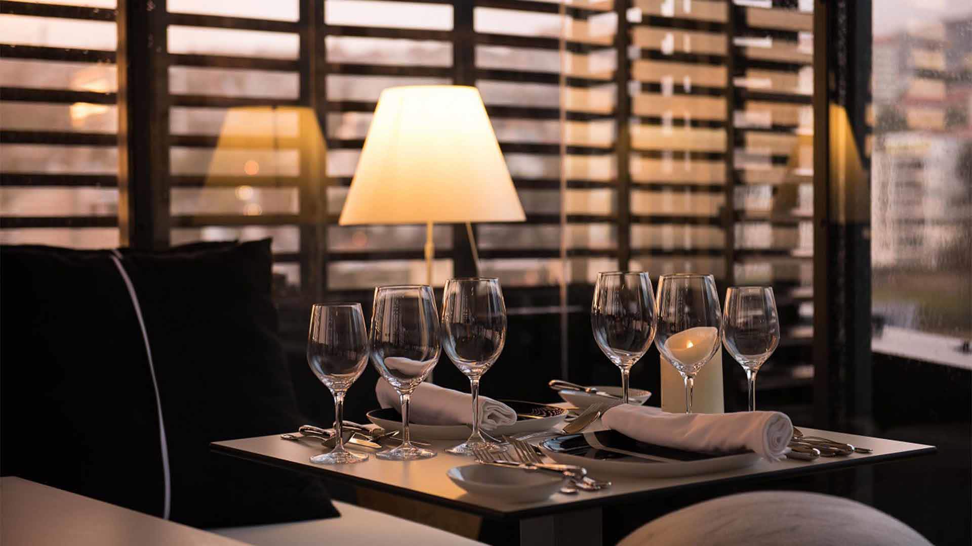 Table with lit lamp and six wine glasses.