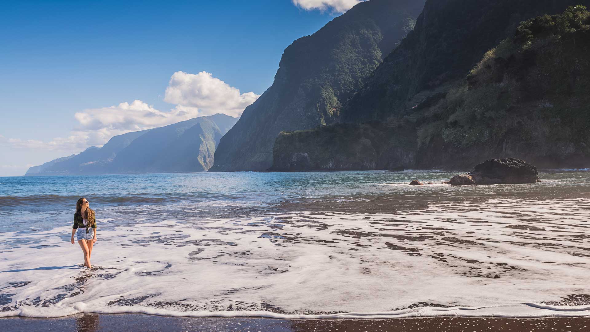 Frau am Meer mit Blick auf das Wasser und die Berge im Hintergrund auf Madeira.