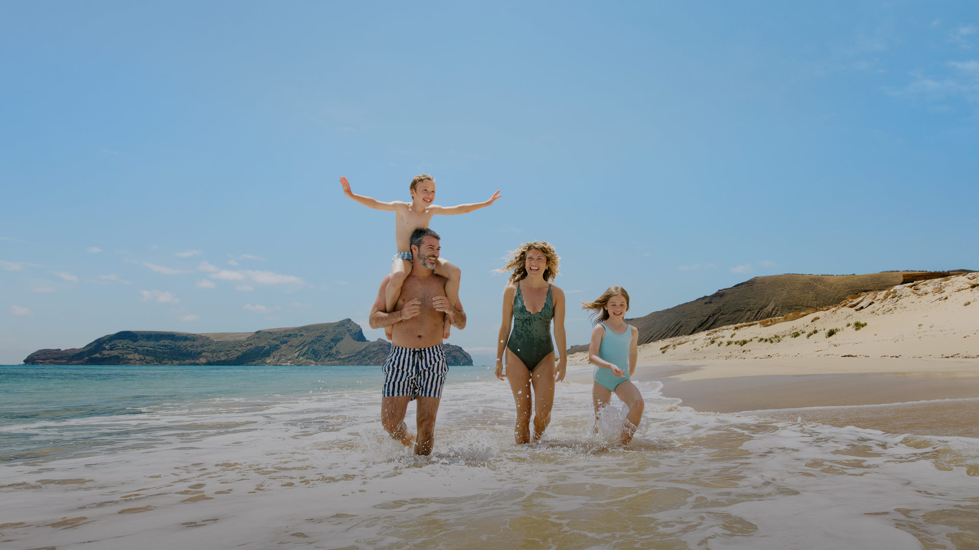 uma família a passear à beira-mar numa praia de areia
