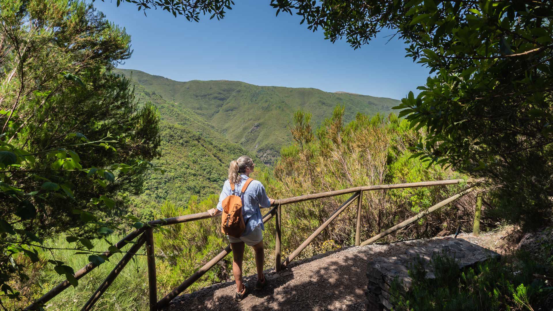 Frau an einem Aussichtspunkt mit Blick auf Berge und Vegetation.