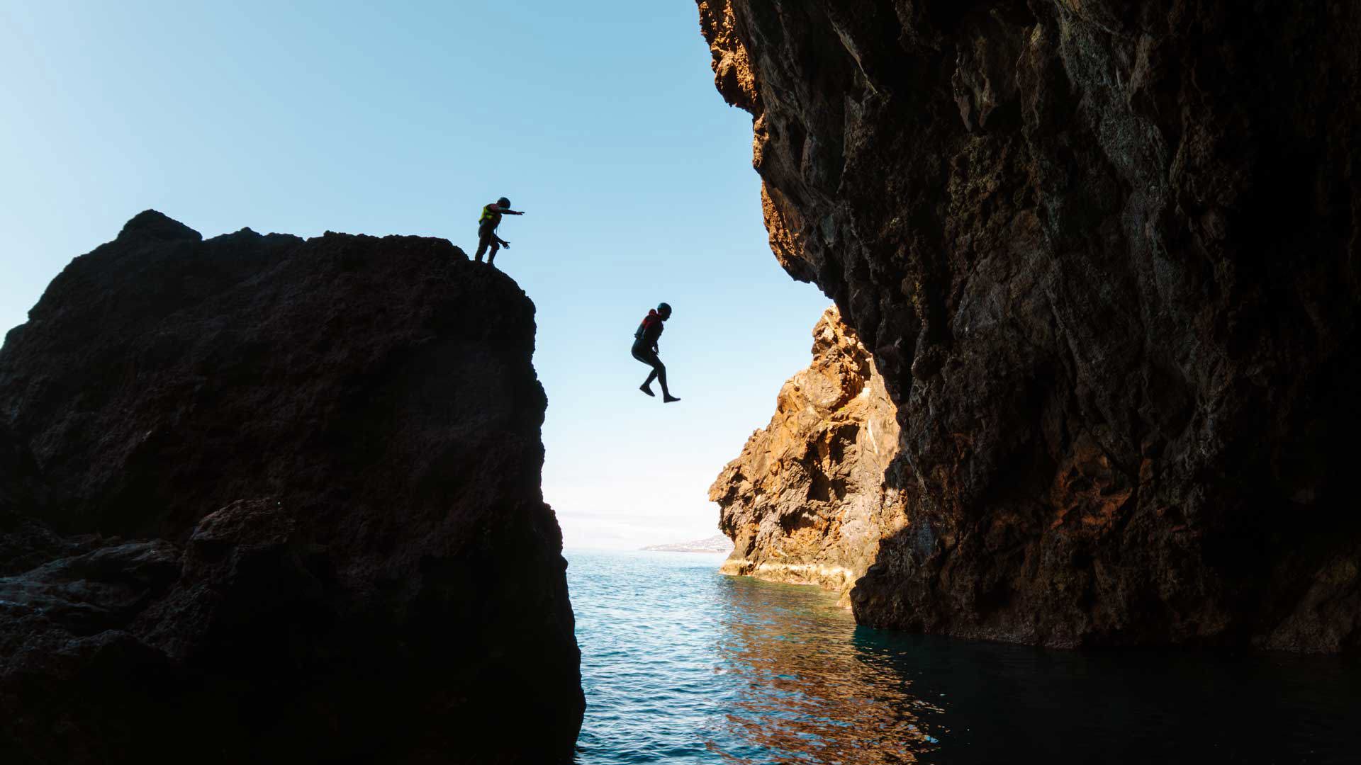 Two people jumping into the sea during a coasteering activity on Madeira Island.