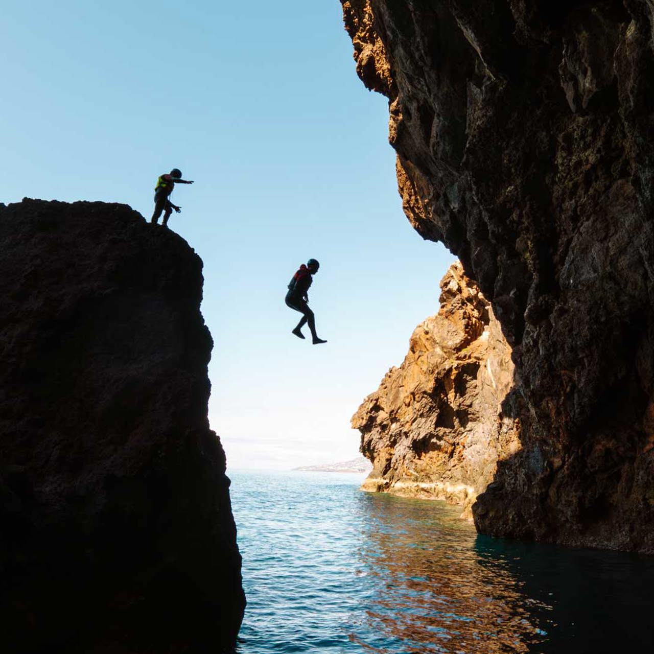 Duas pessoas a saltar para o mar durante uma atividade de coasteering, na Ilha da Madeira.