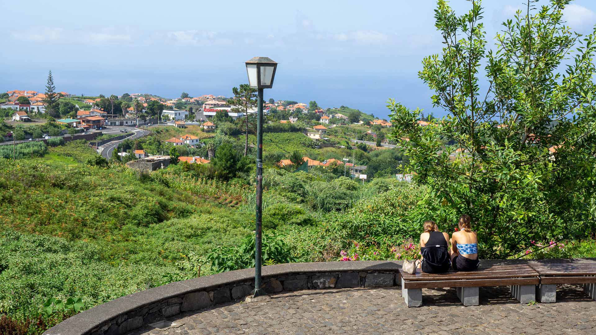 Benches overlooking a green valley and houses in Madeira.
