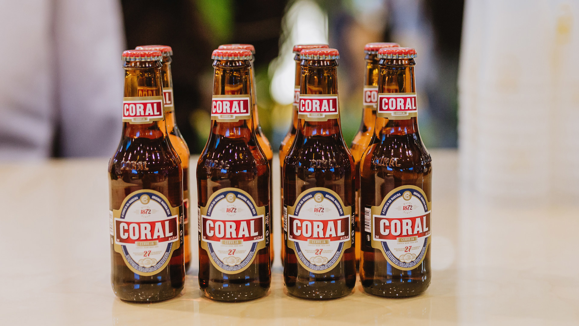 Eight Coral beer bottles lined up on a surface.