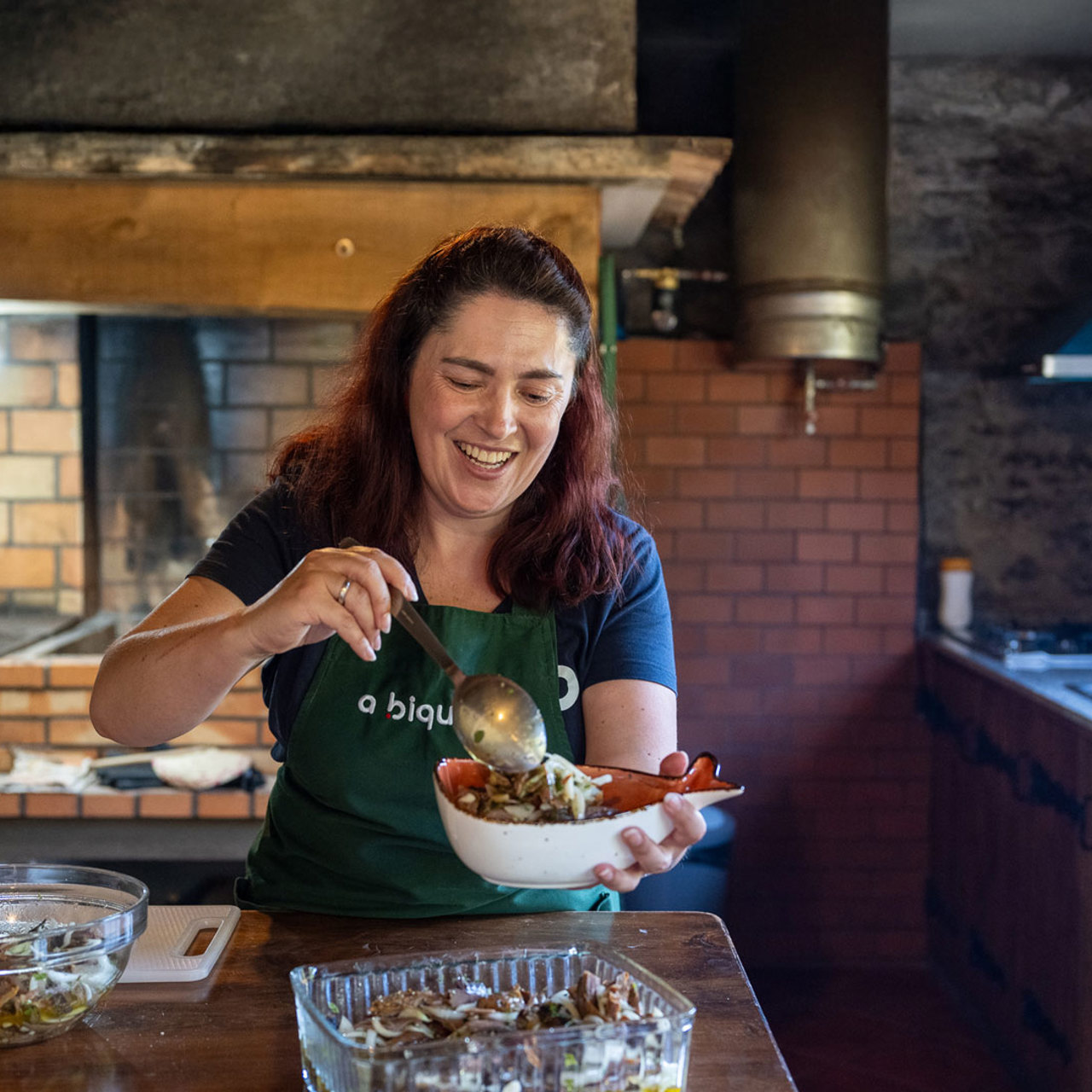 Frau mit Schürze hält eine Schüssel mit Essen.