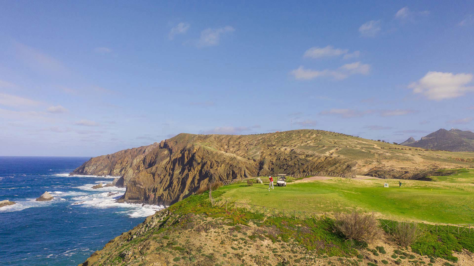 Golfer with buggy on a hillside course by the sea.