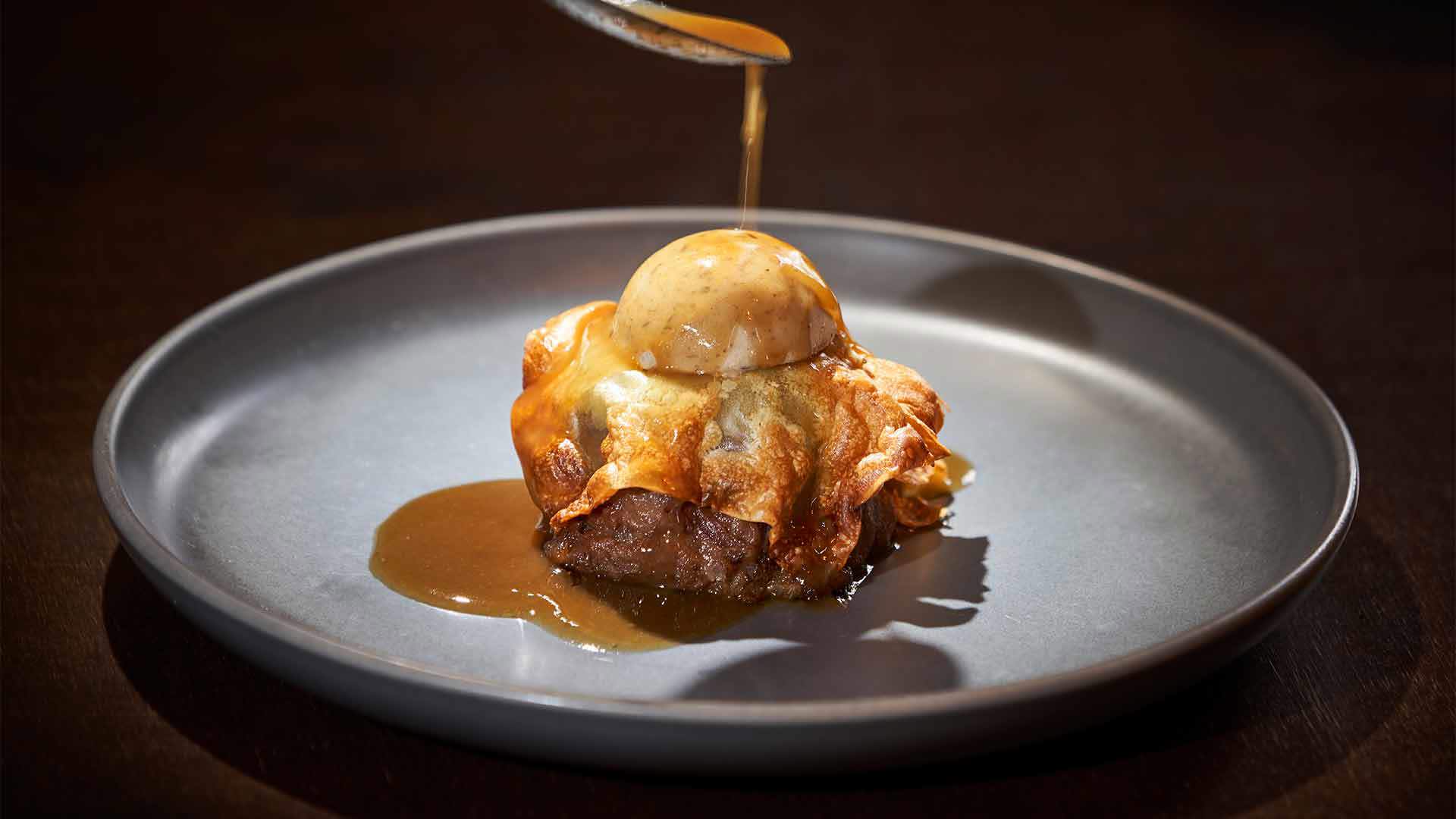 Teller mit bedecktem Steak, das mit Sauce übergossen wird.