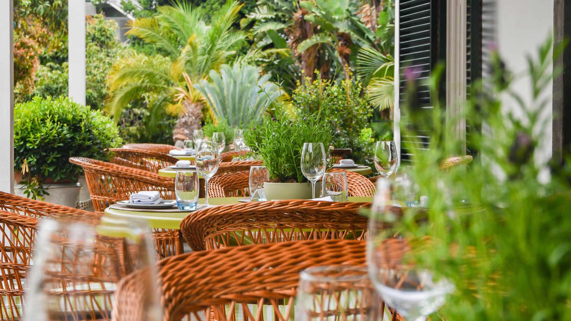 Set tables outdoors at a restaurant, surrounded by plants.