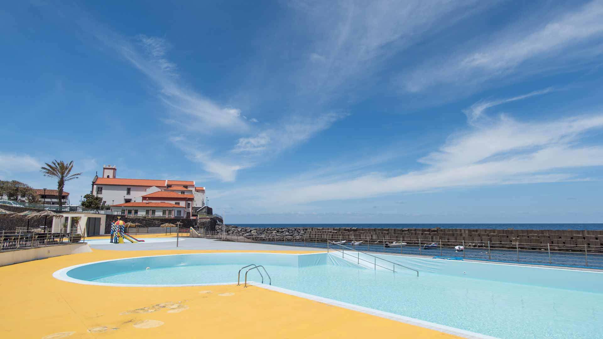 Piscina com céu azul e casas ao fundo na Madeira.