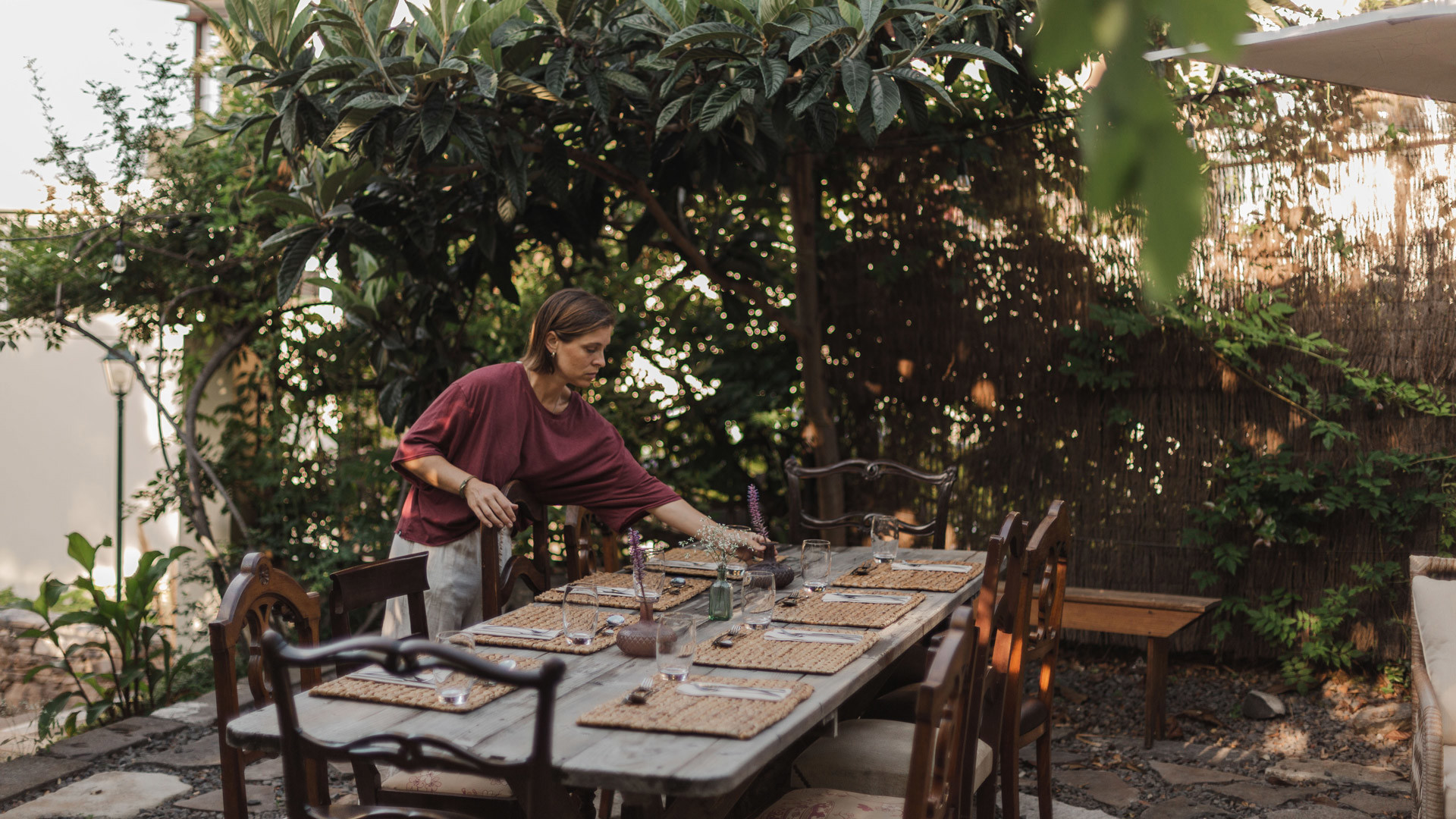 Frau deckt den Tisch im Freien mit Baum in der Nähe.