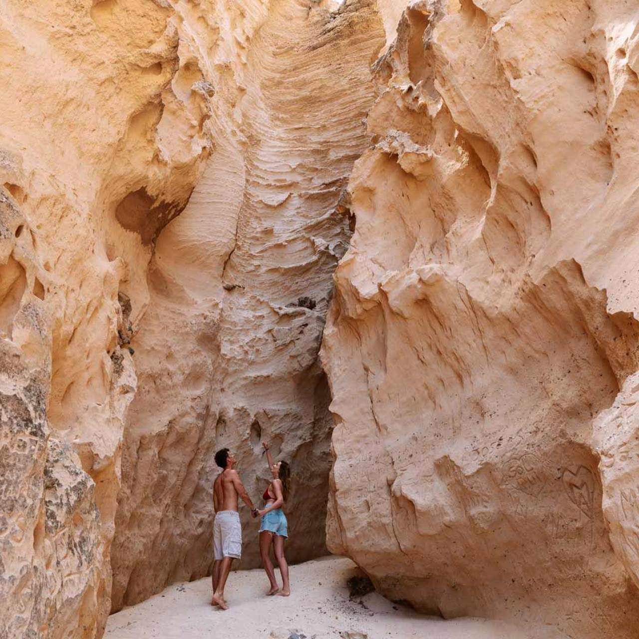 Casal junto a fenda geológica em área arenosa