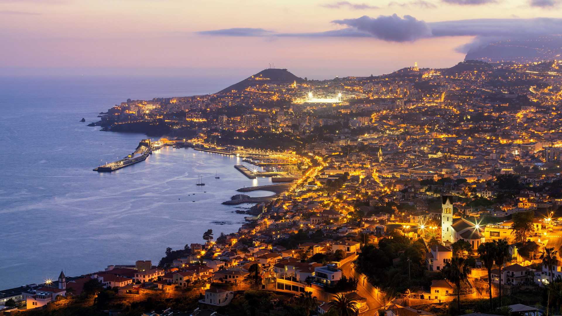 Sunset by the sea with lights along Madeira’s coast.