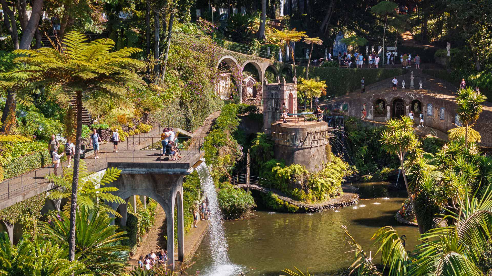 Lac avec fontaines et visiteurs au Jardin Tropical Monte Palace Madeira, entouré de végétation.