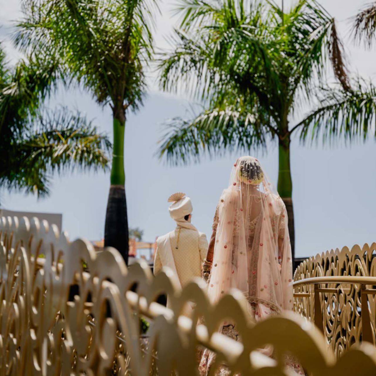 Casal em trajes de casamento sobre uma ponte rodeada de palmeiras.